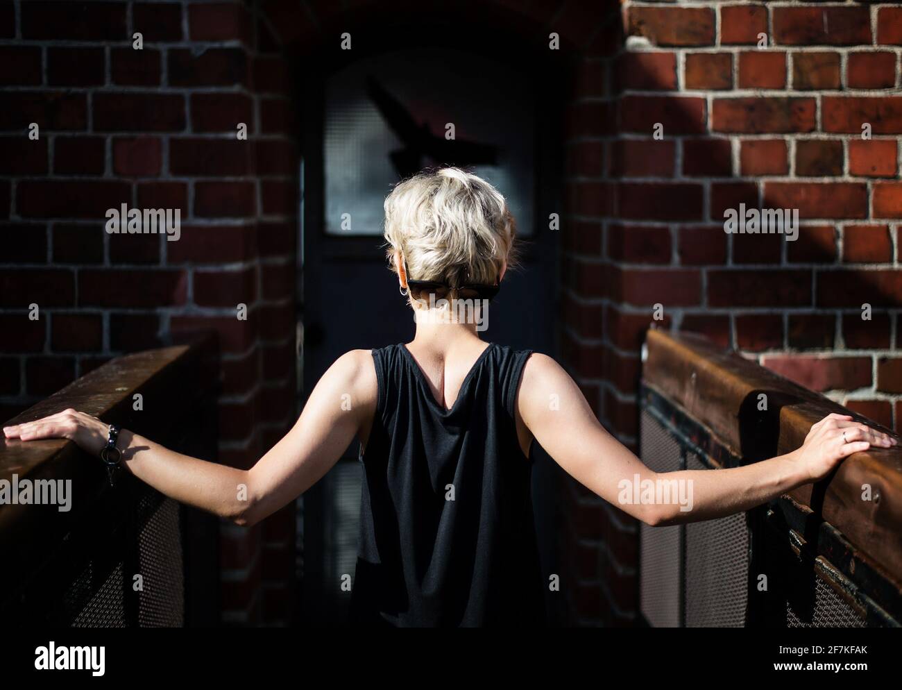 femme blonde de cheveux dans une robe noire debout avec son dos sur un pont contre avec mur de brique. Jeune femme élégante marchant dans la rue de la ville Banque D'Images