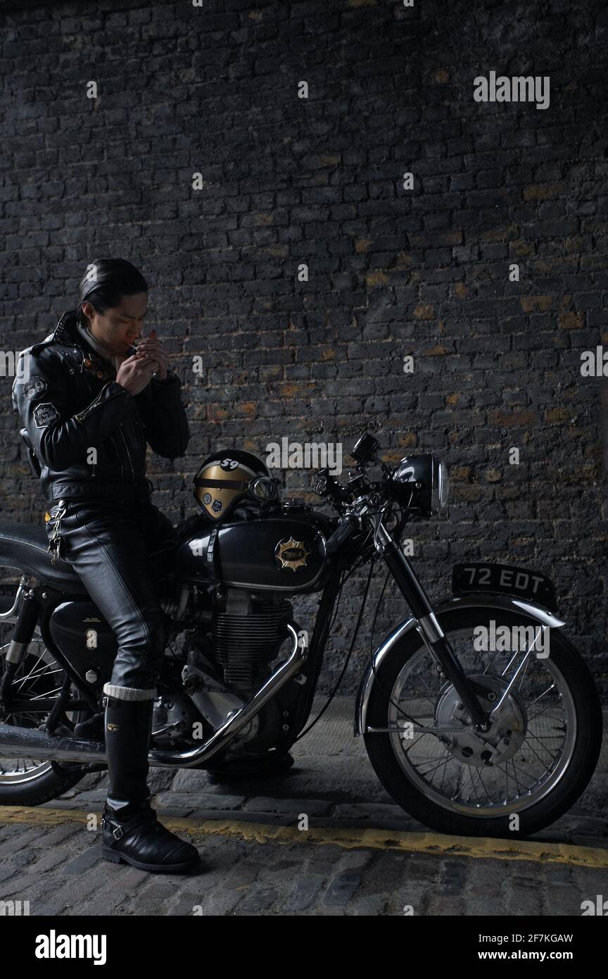 biker , coureur de café portant une veste en cuir noir assis sur une moto britannique classique et fuyant une cigarette à Londres, Royaume-Uni Banque D'Images