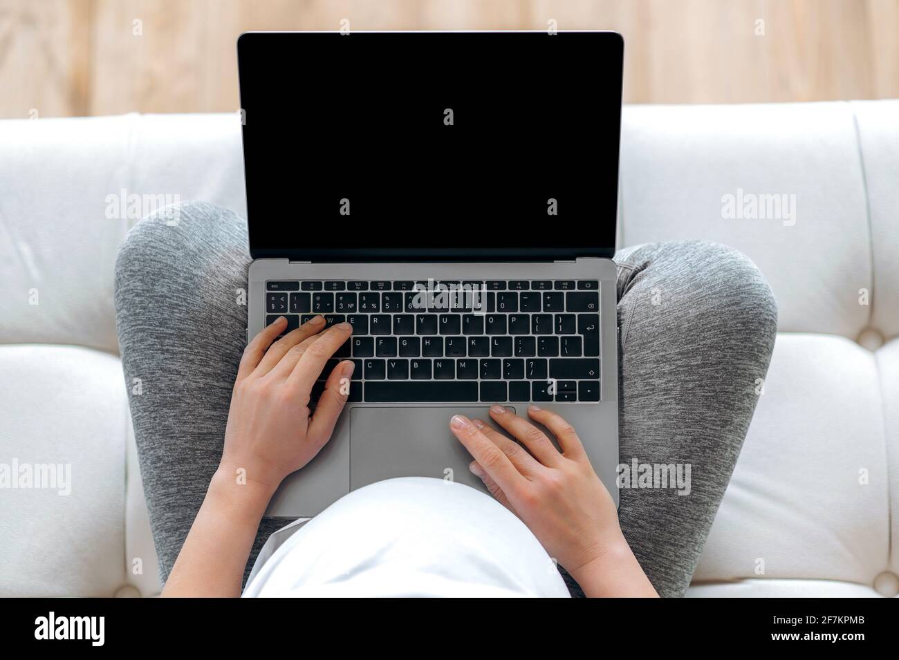 Concept de technologie, gadget sans fil. Vue de dessus de la femme enceinte en t-shirt blanc assis sur un canapé, tenant un ordinateur portable avec écran noir vide en main, lieu pour votre présentation Banque D'Images
