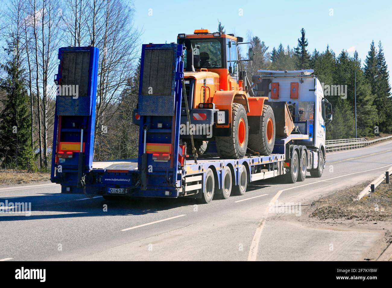 Le camion transporte une chargeuse sur pneus Doosan sur une remorque basse longueur le long de l'autoroute, un beau jour de printemps, vue arrière. Jokioinen, Finlande. 1er avril 2021. Banque D'Images