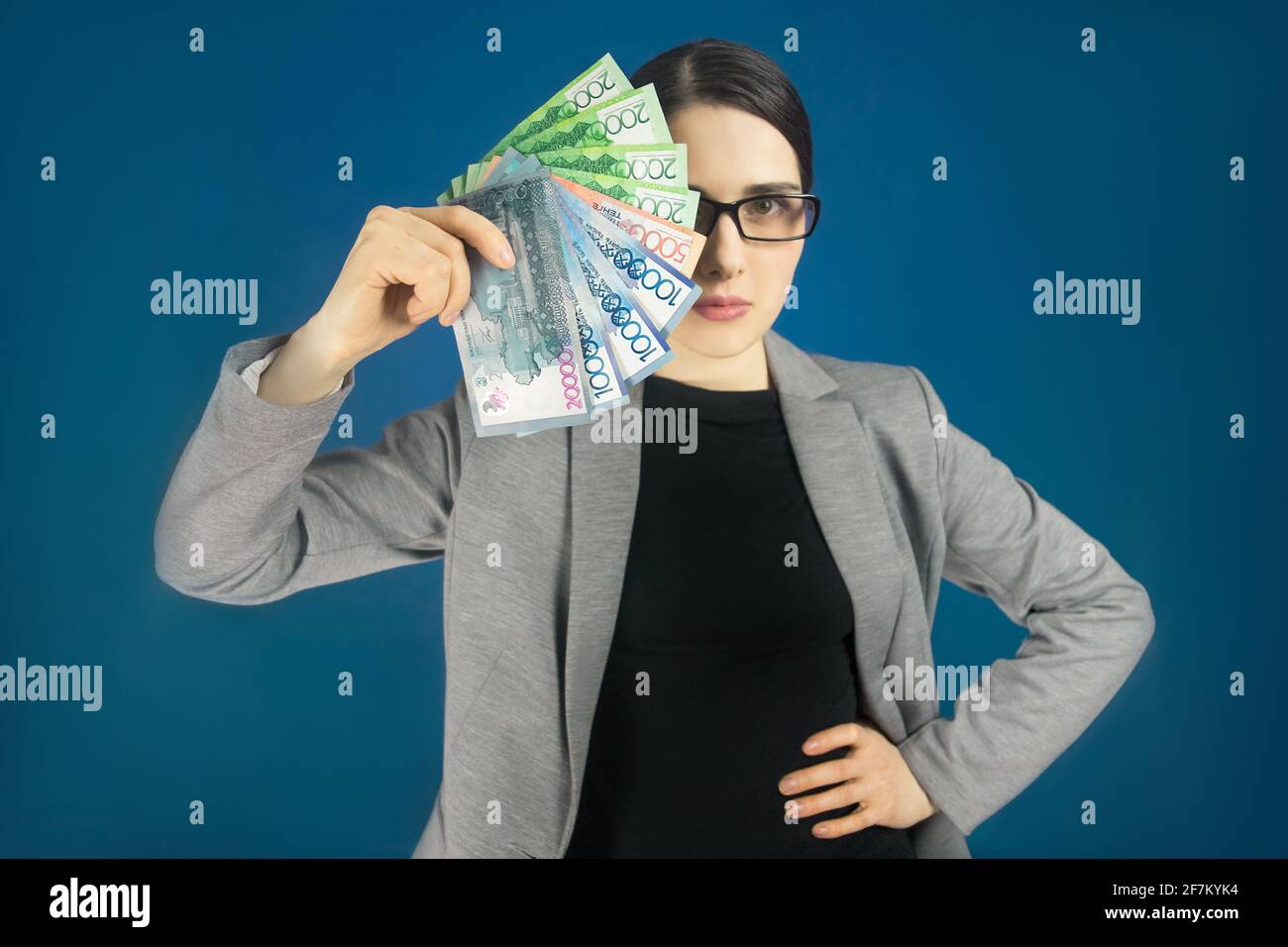 Femme regardant la caméra avec l'argent kazakhri tenge dans sa main. Couvre la moitié du visage avec des billets. Banque D'Images