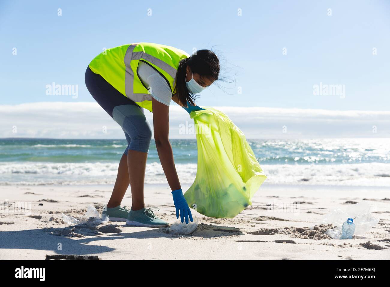 Femme de race mixte portant un masque facial collectant des déchets de la plage Banque D'Images