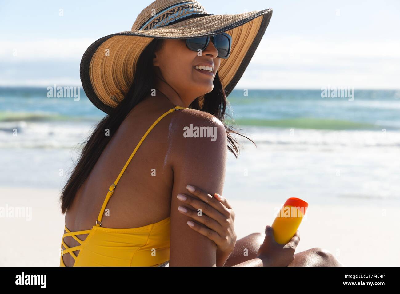 Femme de course mixte souriante pendant les vacances à la plage en utilisant de la crème solaire Banque D'Images