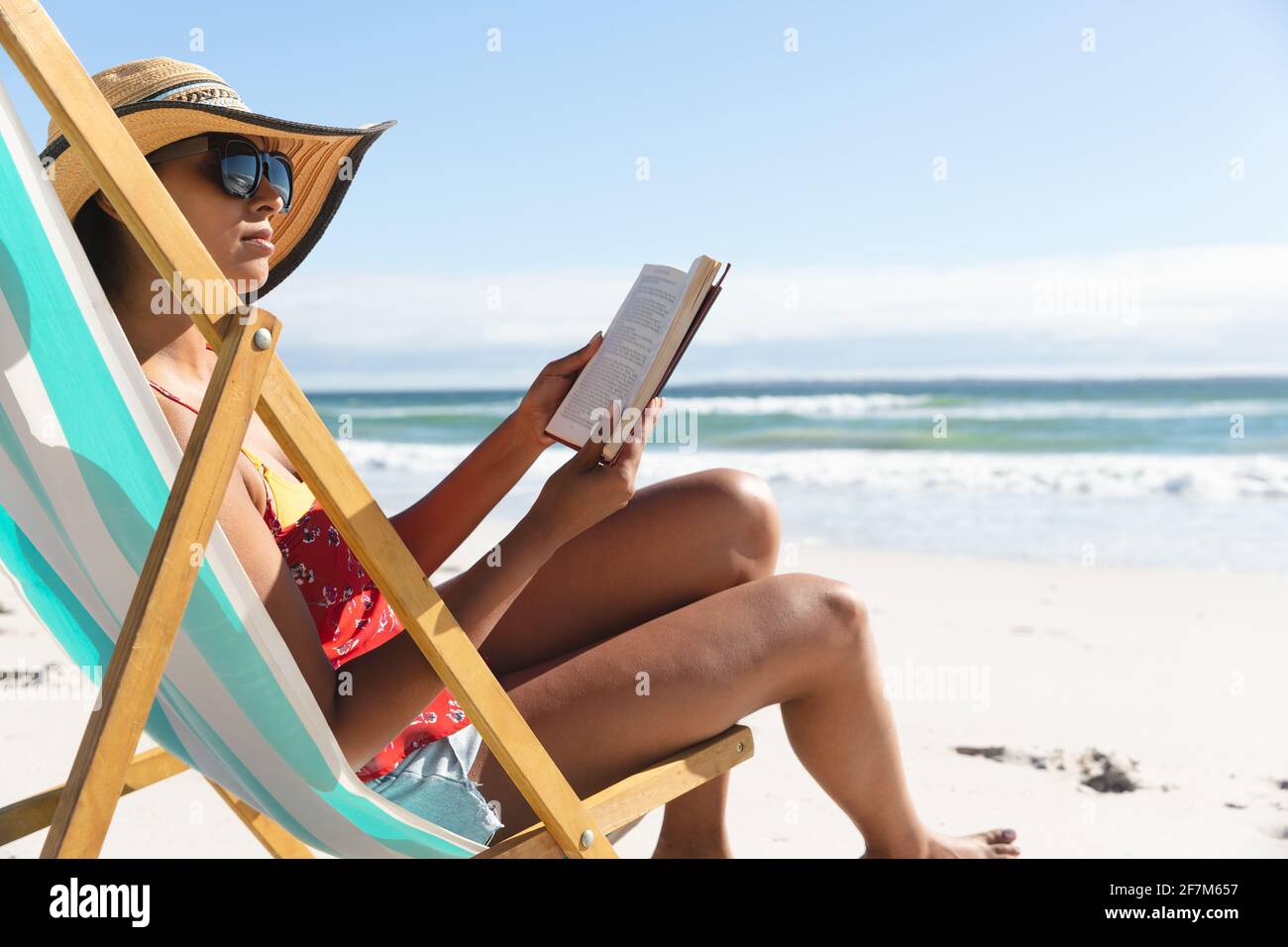 Femme de race mixte sur la plage de vacances assis dans le transat de lecture livre Banque D'Images