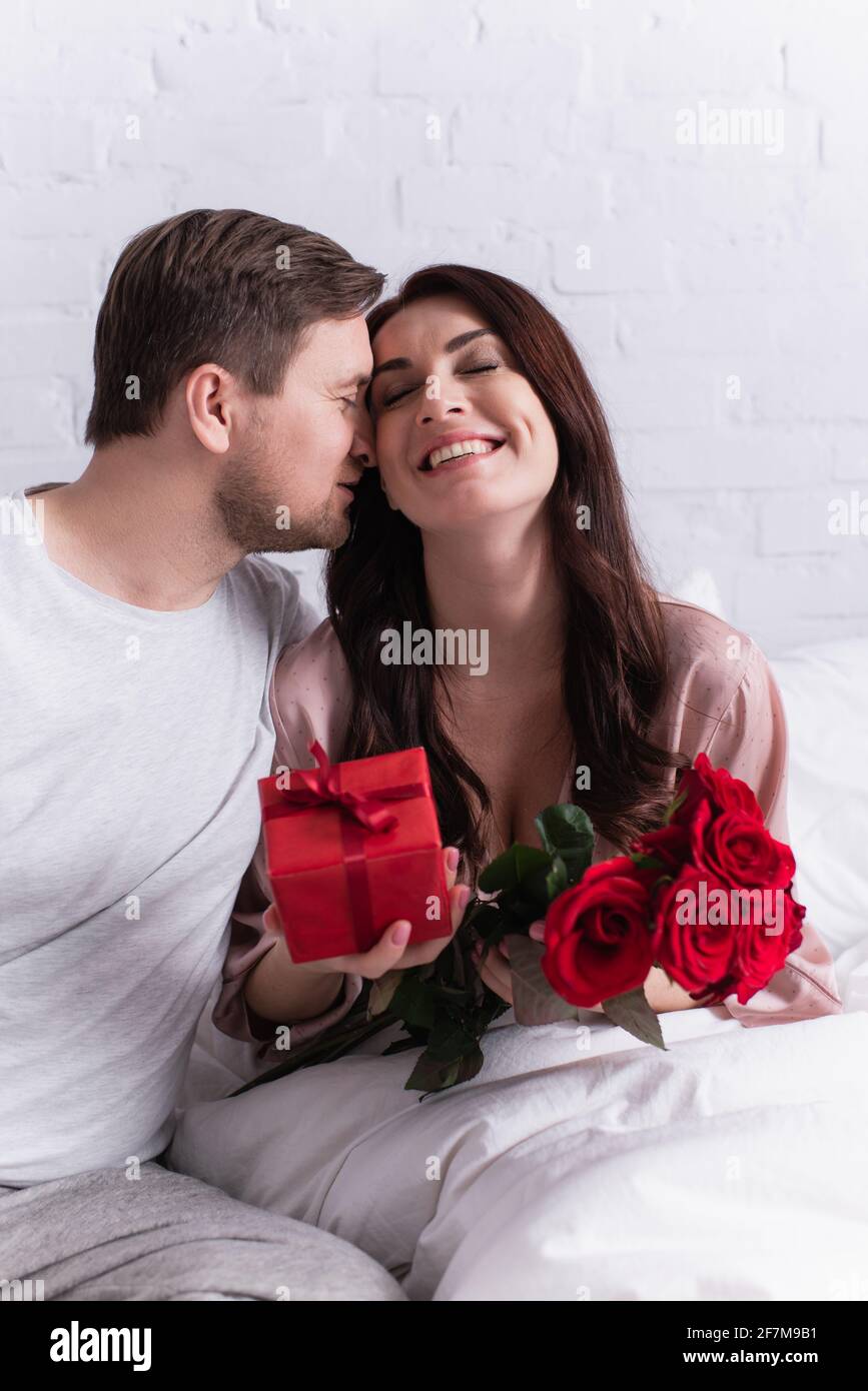 Homme embrassant la femme heureuse avec des roses et des fleurs sur flou premier plan dans la chambre Banque D'Images