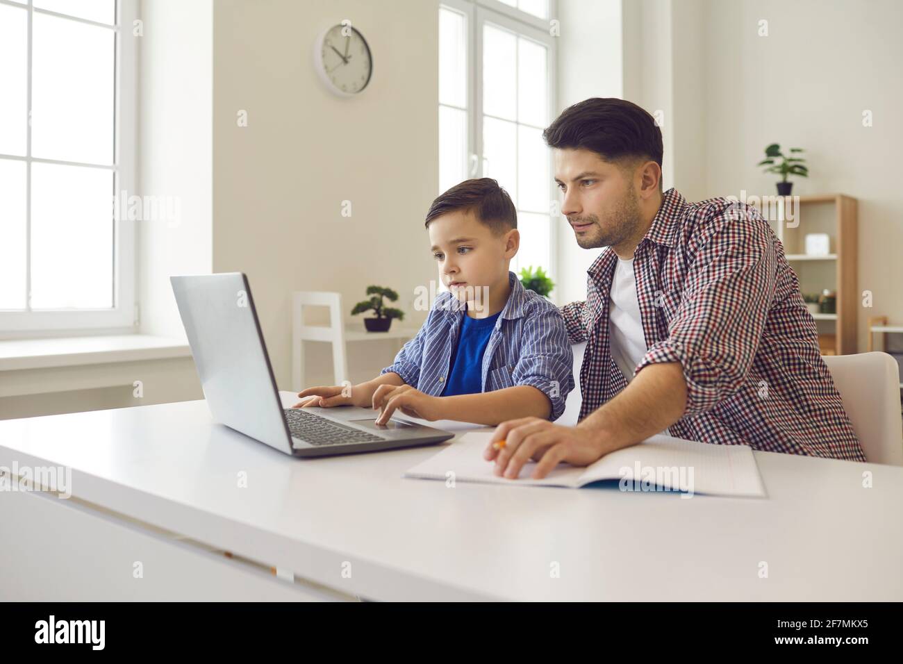 Un père de race blanche aide son fils à faire ses devoirs en ligne assis à son bureau avant de l'ordinateur portable Banque D'Images