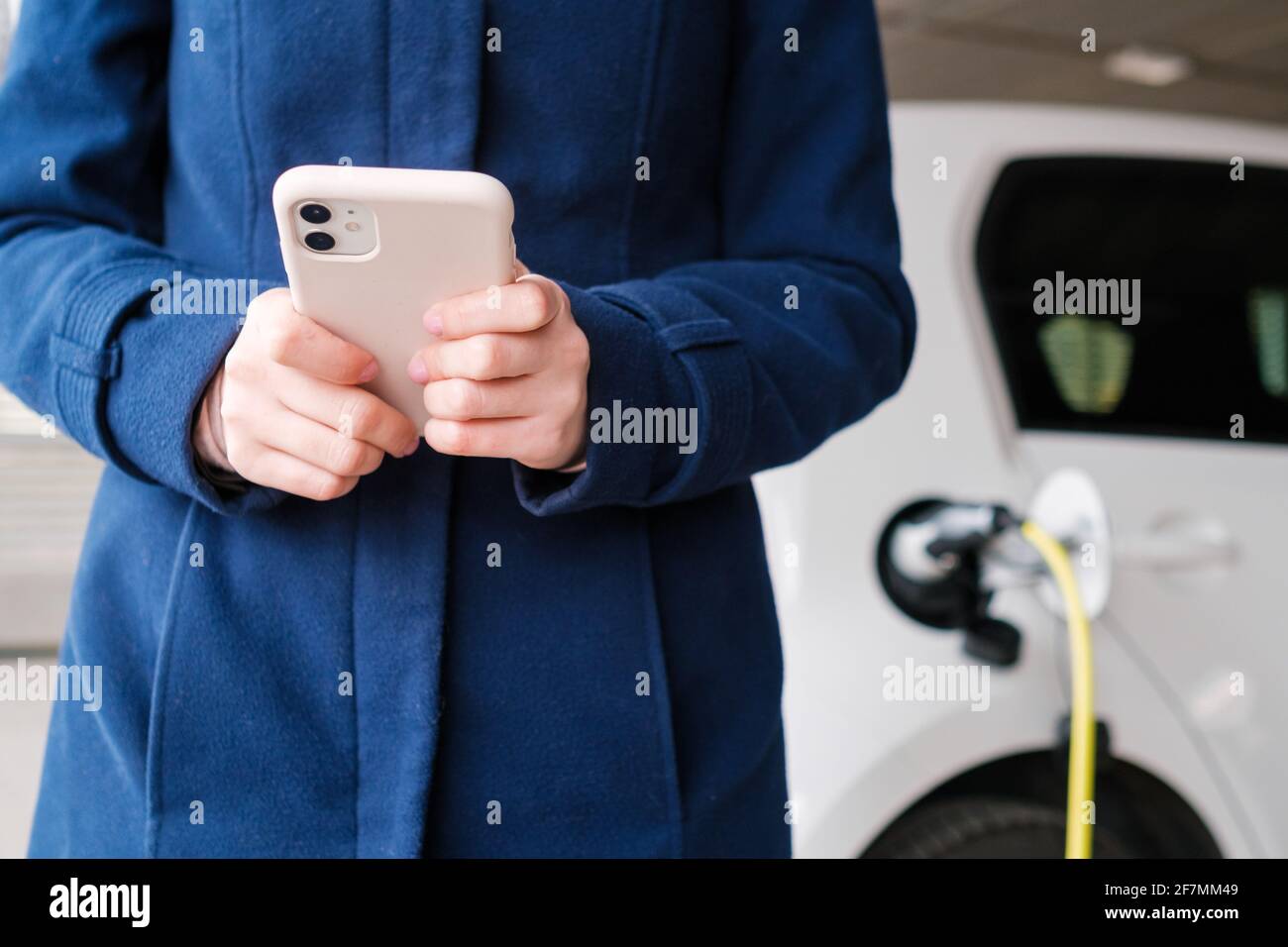 Femme utilisant son téléphone portable sur l'arrière-plan de chargement de la voiture électrique au parking Banque D'Images