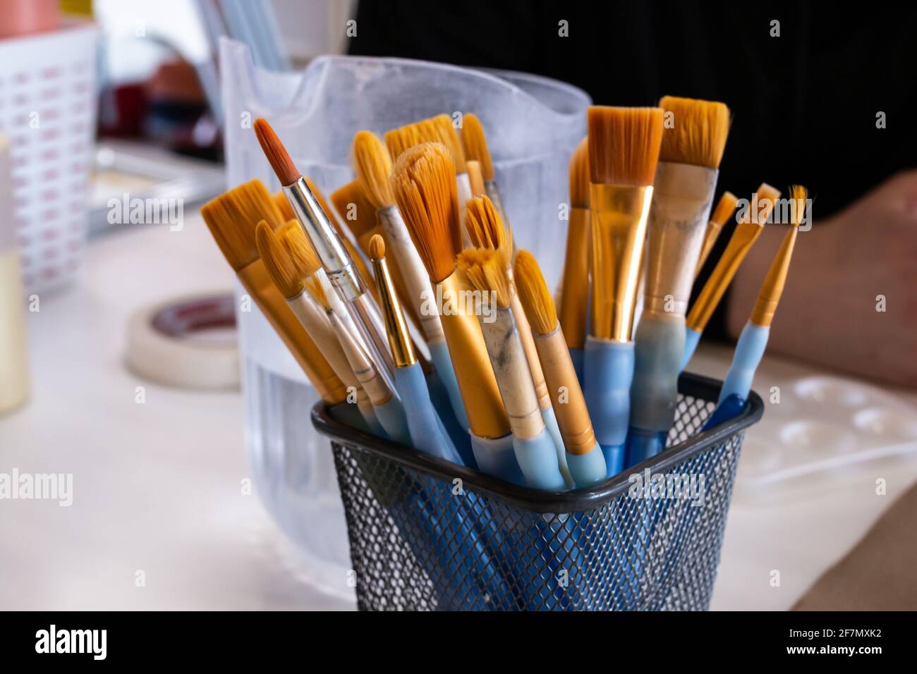 Un support en métal rempli de pinceaux à bout jaune de différentes tailles sur une table d'artiste à côté d'un pichet d'eau à London, Ontario, Canada. Banque D'Images