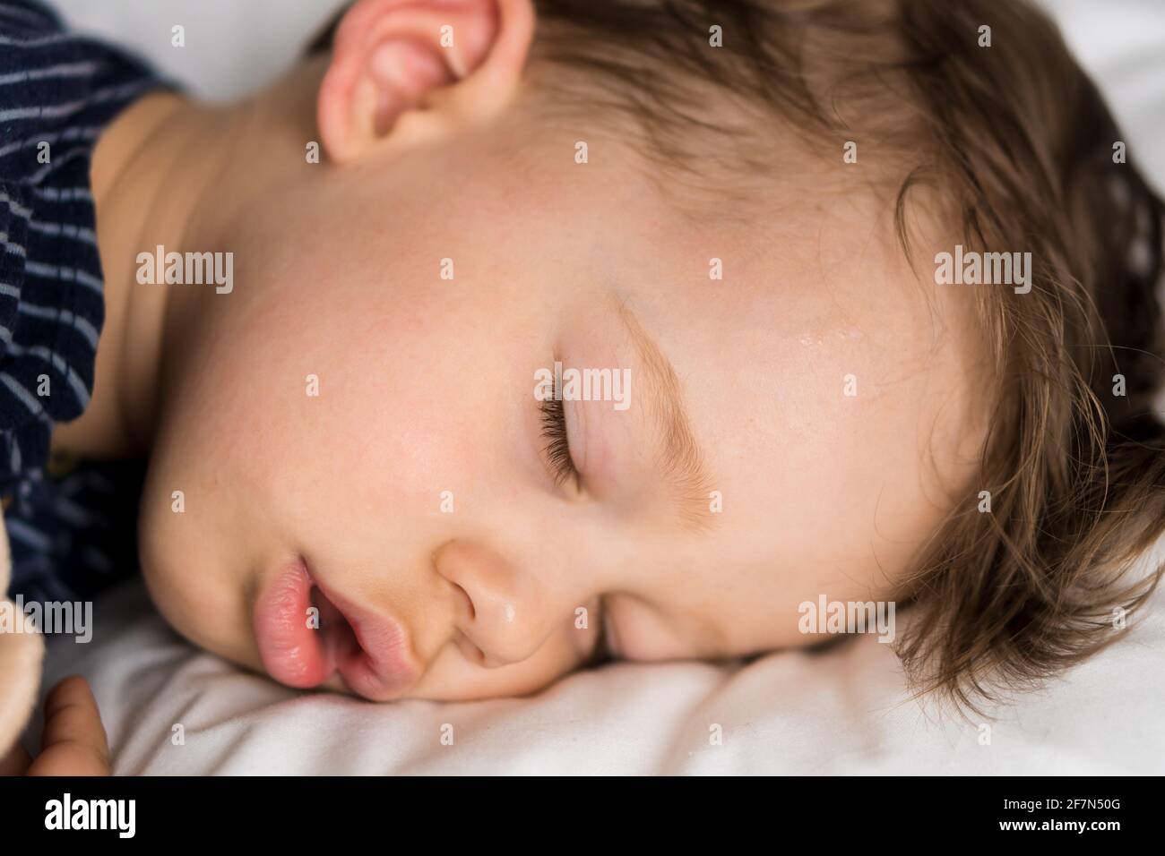 Portrait authentique malade mignon petit petit garçon d'âge préscolaire caucasien dans le sommeil bleu avec l'ours en peluche sur le lit blanc. Enfant reposant à l'heure du déjeuner. Soins Banque D'Images