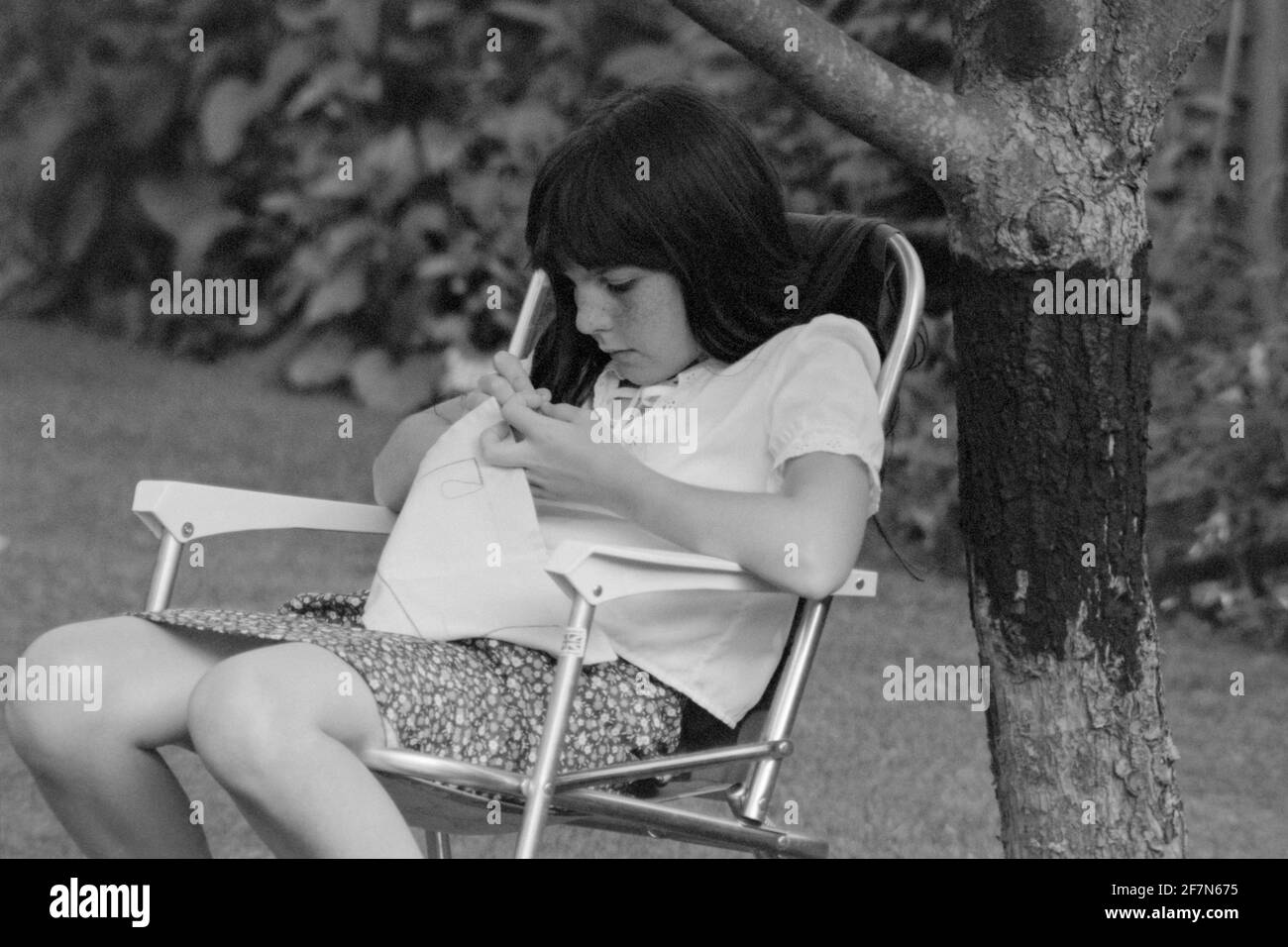 jeune fille se concentrant sur la couture dans le jardin early1980 royaume-uni Banque D'Images