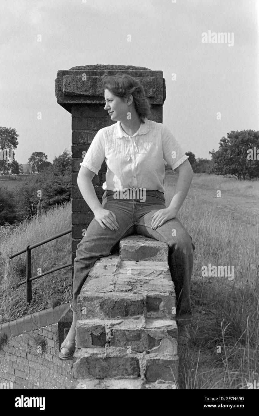 jeune jolie femme assise precarily sur le parapet de pont disused pendant vue sur le paysage rural environnant début des années 1980 angleterre royaume-uni Banque D'Images