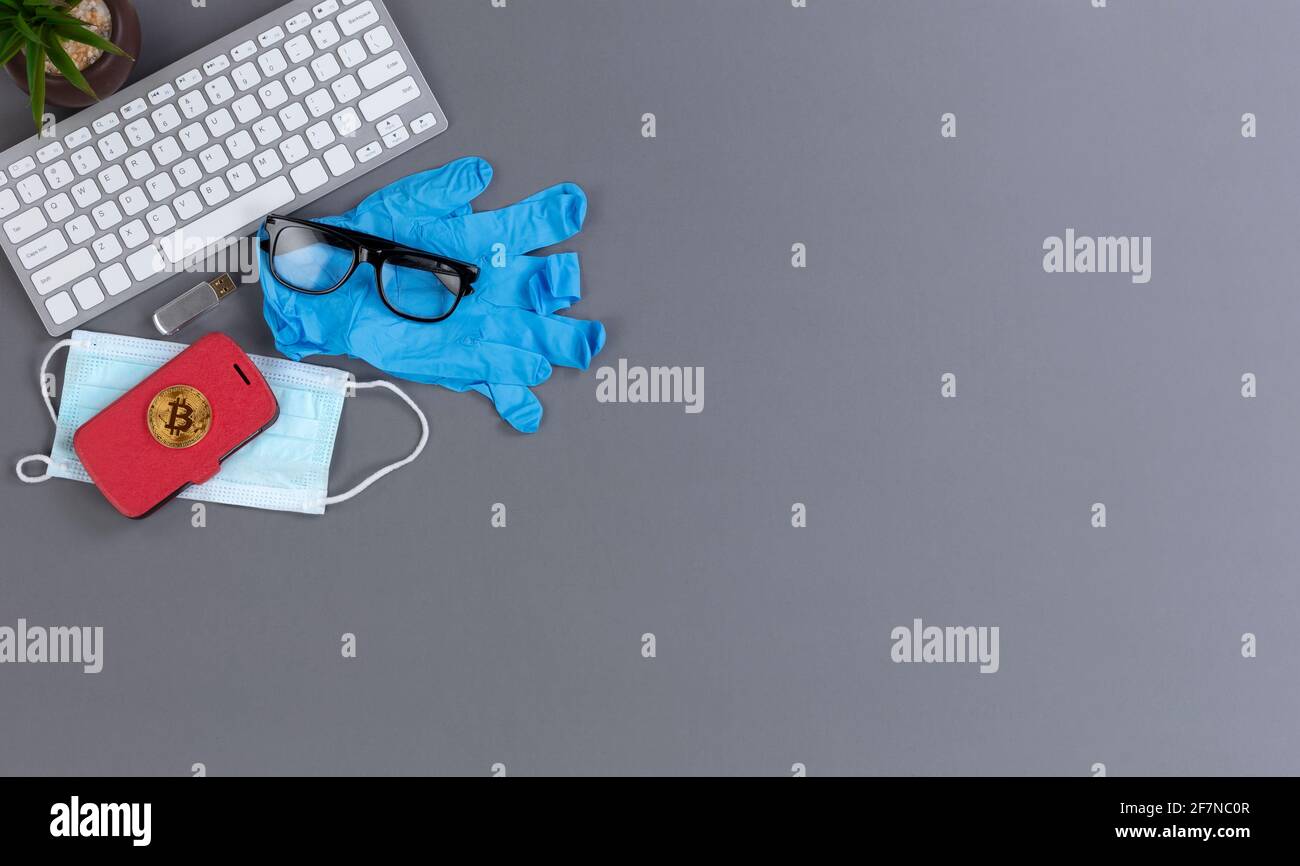 Concept de retour au travail pendant le coronavirus ou la pandémie Covid 19 avec masque facial, smartphone, bitcoin et gants sur le dessus du clavier d'ordinateur Banque D'Images