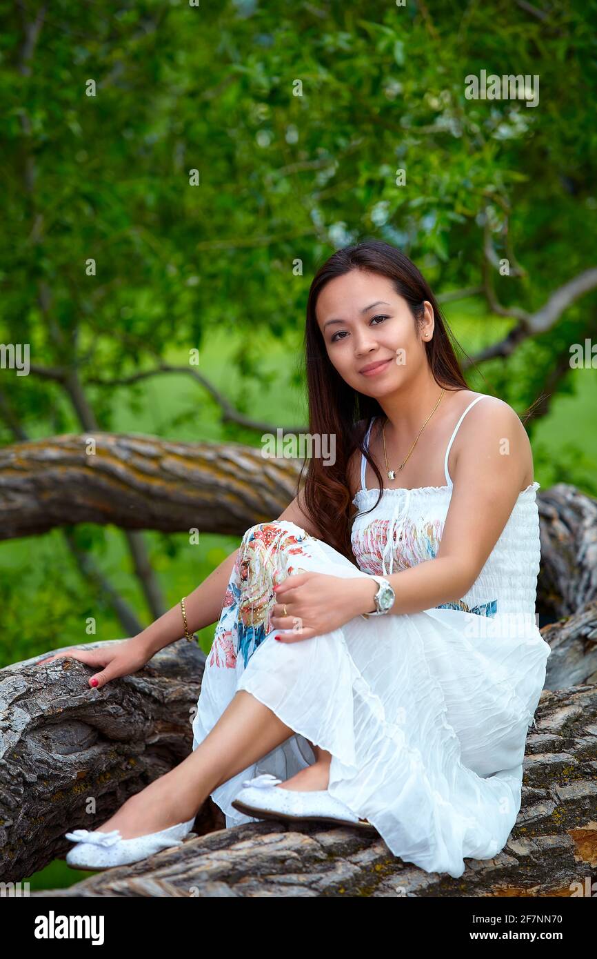 Femme philippine adulte en robe regardant l'appareil photo tout en vous relaxant sur le tronc de l'arbre le jour de l'été forêt Banque D'Images