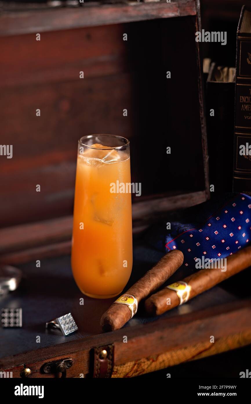 Un cocktail fruité et fort servi dans un grand verre de glace, exposé avec deux cigares et des boutons de manchette pour la fête des pères. Banque D'Images