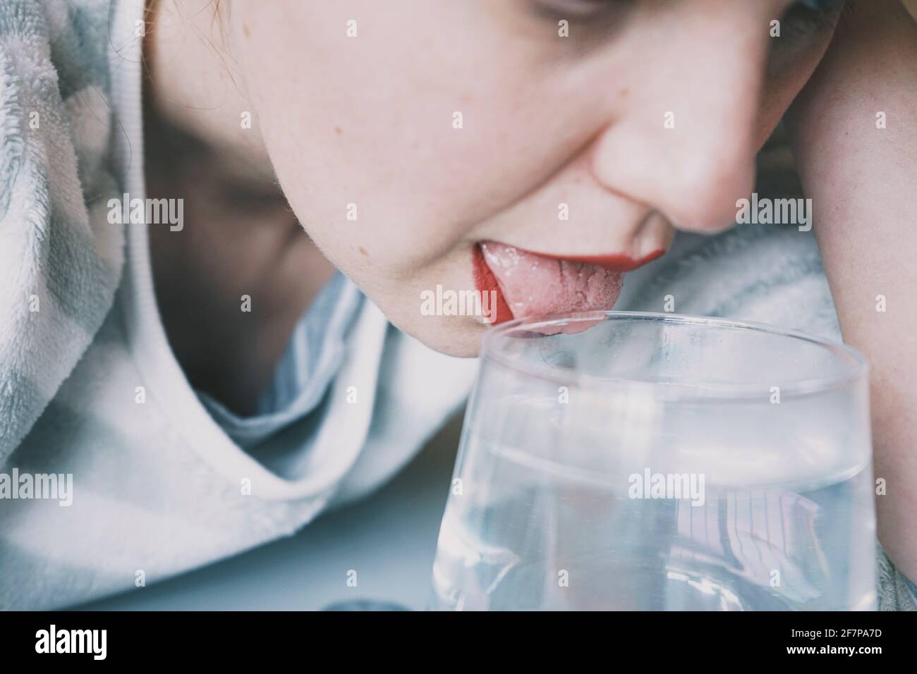 Portrait d'une jeune femme cachée par un verre avec une boisson transparente Banque D'Images