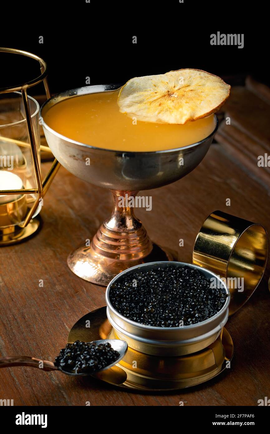 Un cocktail fruité et joyeux servi dans un coupé shinny doré avec une tranche de pomme et un caviar délicieux et cher Banque D'Images