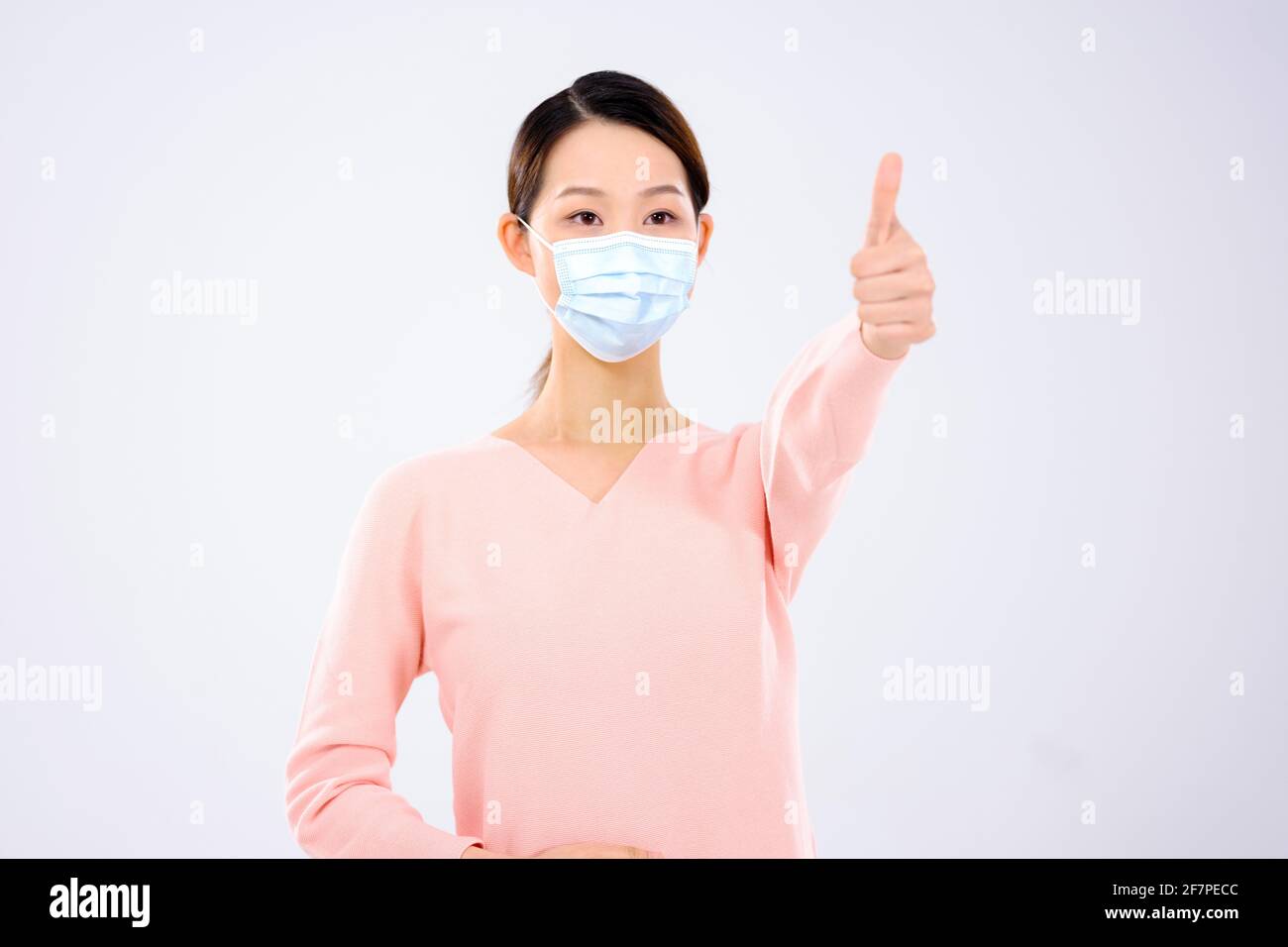 Une jeune femme avec un masque a tenu son pouce sourire Banque D'Images