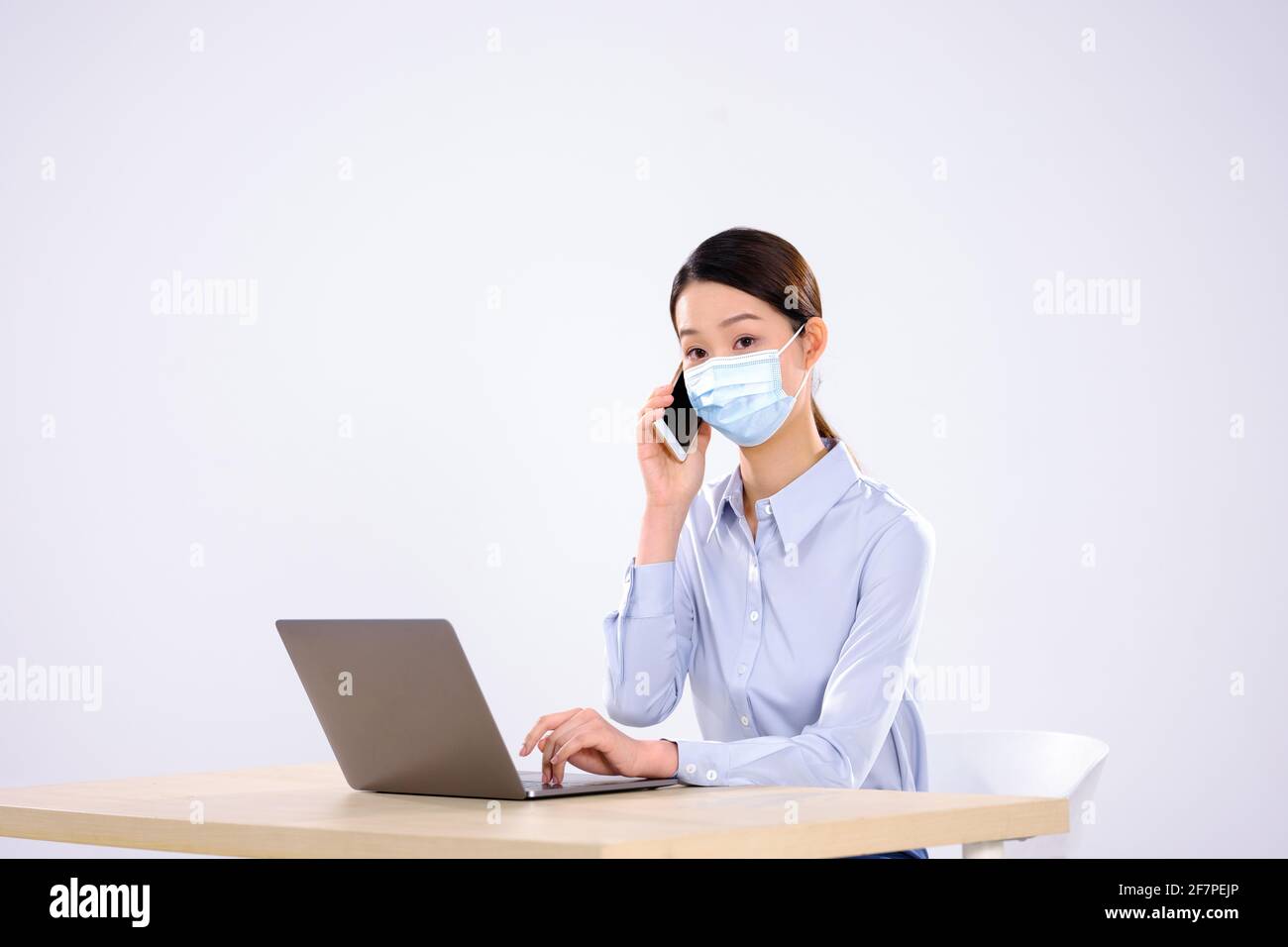 Une jeune femme avec un masque est au téléphone dans la vue latérale du bureau Banque D'Images