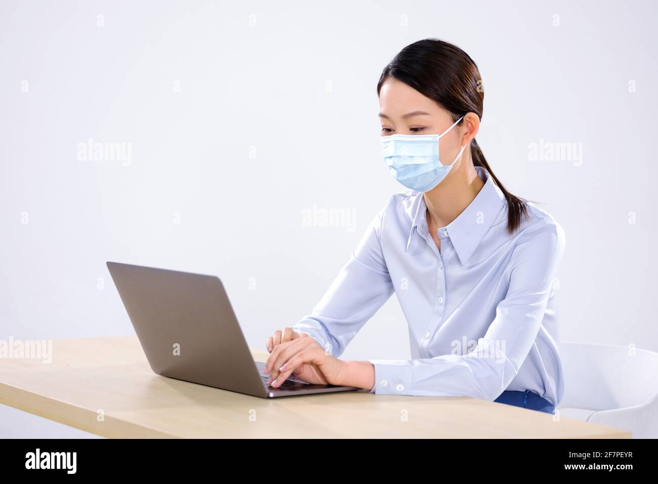 Une jeune femme avec un masque utilise un ordinateur portable dans le bureau ne regardant pas la caméra Banque D'Images