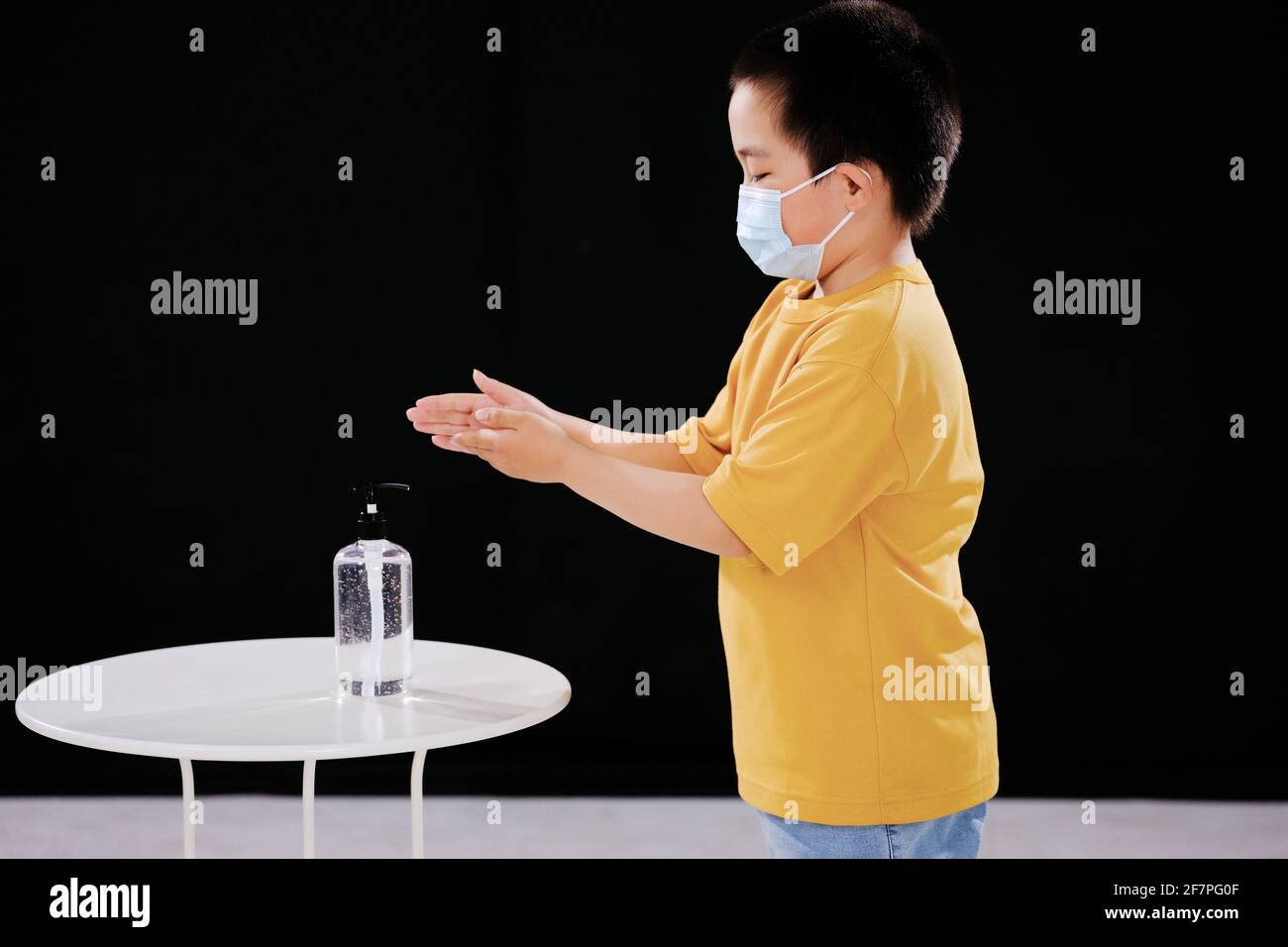 Un petit garçon avec un masque utilise un désinfectant pour les mains Banque D'Images