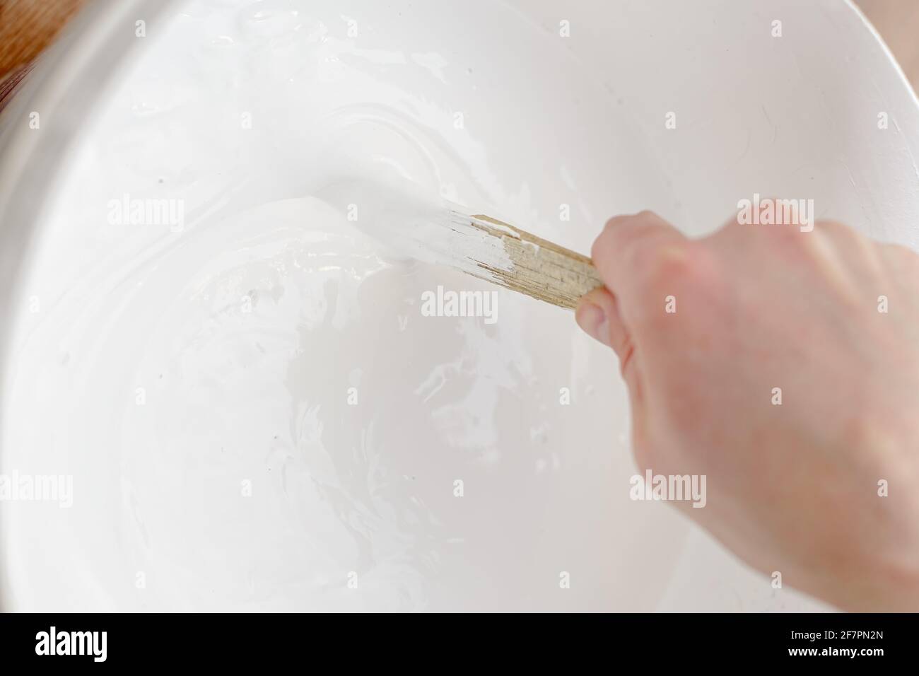 La main de peintre mélange la peinture blanche dans le pot avec un bâton de bois. Réparations à domicile. Banque D'Images