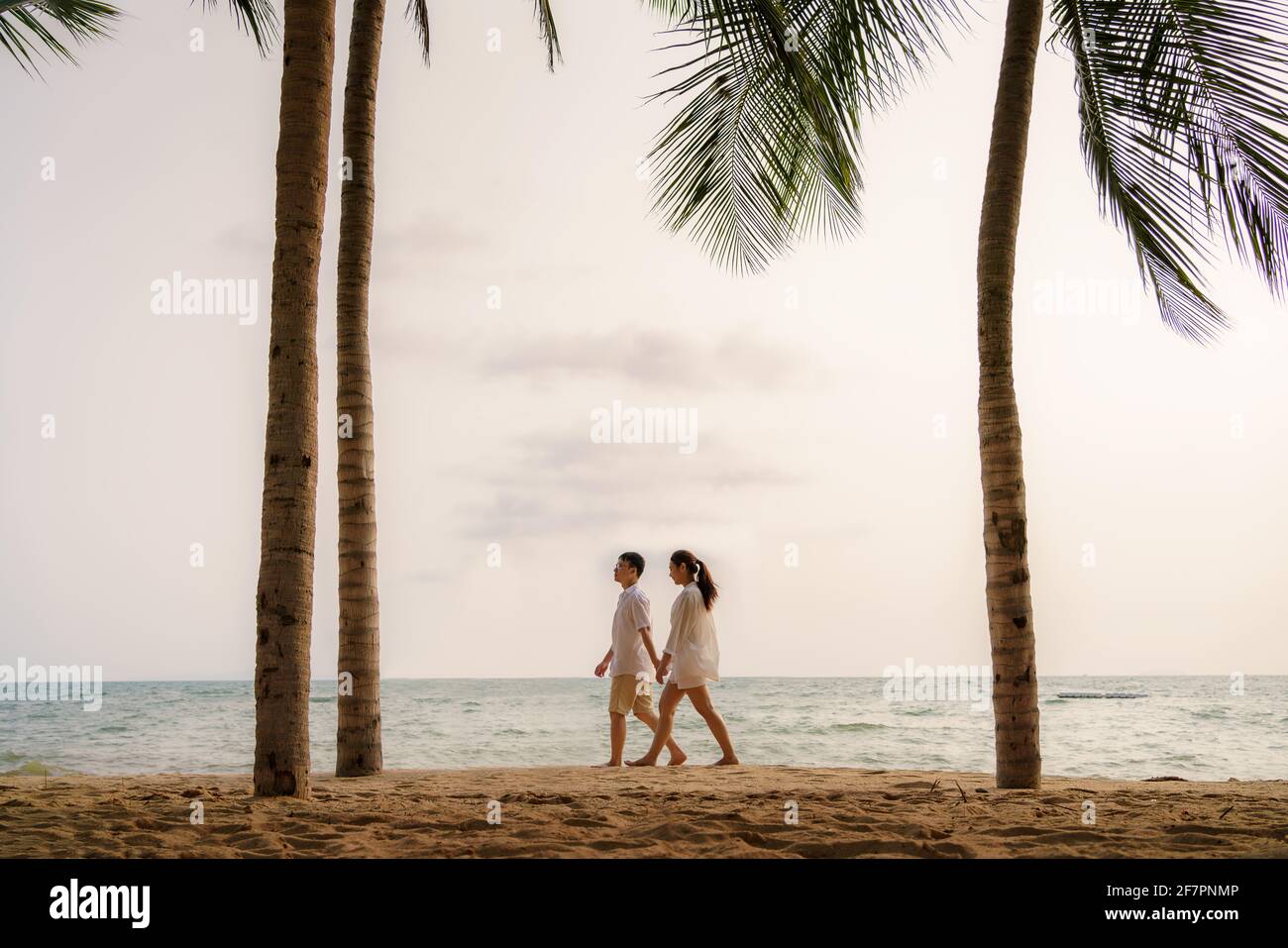 Le couple asiatique marche et tient la main sur une plage de front de mer avec des cocotiers pendant les vacances en été en Thaïlande. Banque D'Images