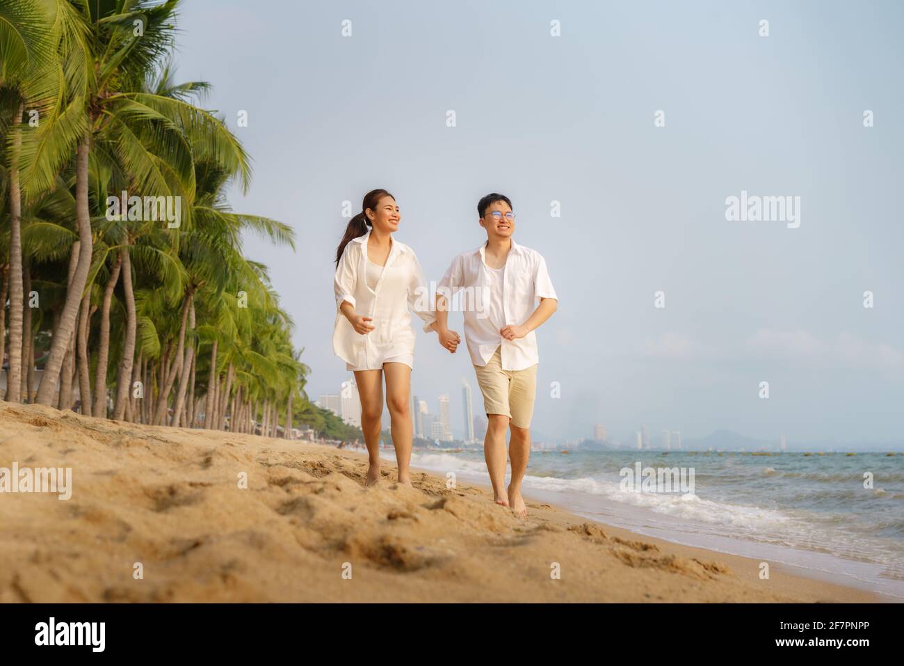 Le couple asiatique court et tient la main sur une plage de front de mer avec des cocotiers pendant les vacances en été en Thaïlande. Banque D'Images