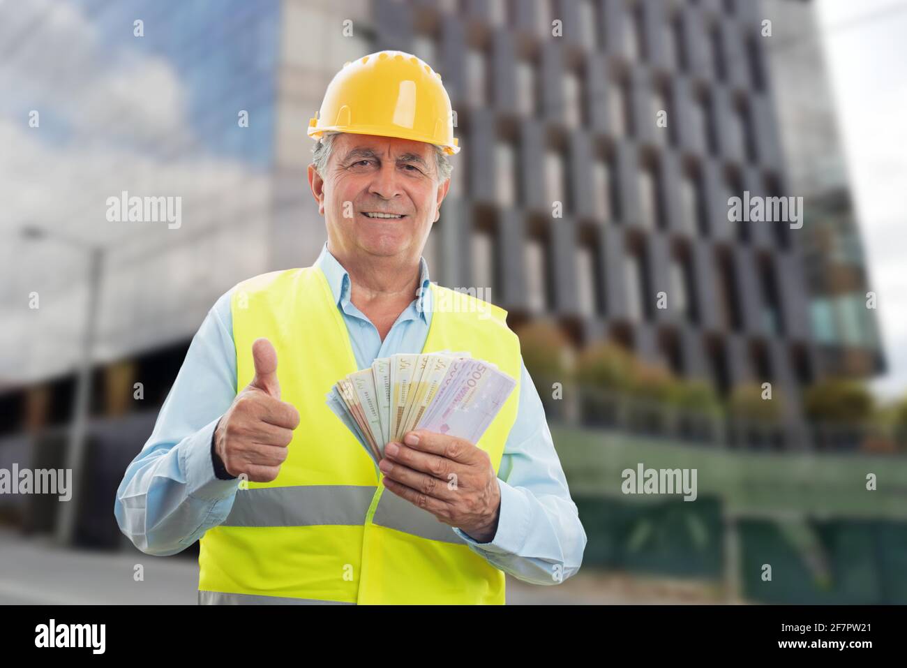 Joyeux Homme De Constructeur Age Portant Gilet Et Chapeau Jaune Souriant Tenir De L Argent Comptant Montrant Le Pouce Vers Le Haut Comme Un Geste Comme Le Concept De Salaire Avec Bac De
