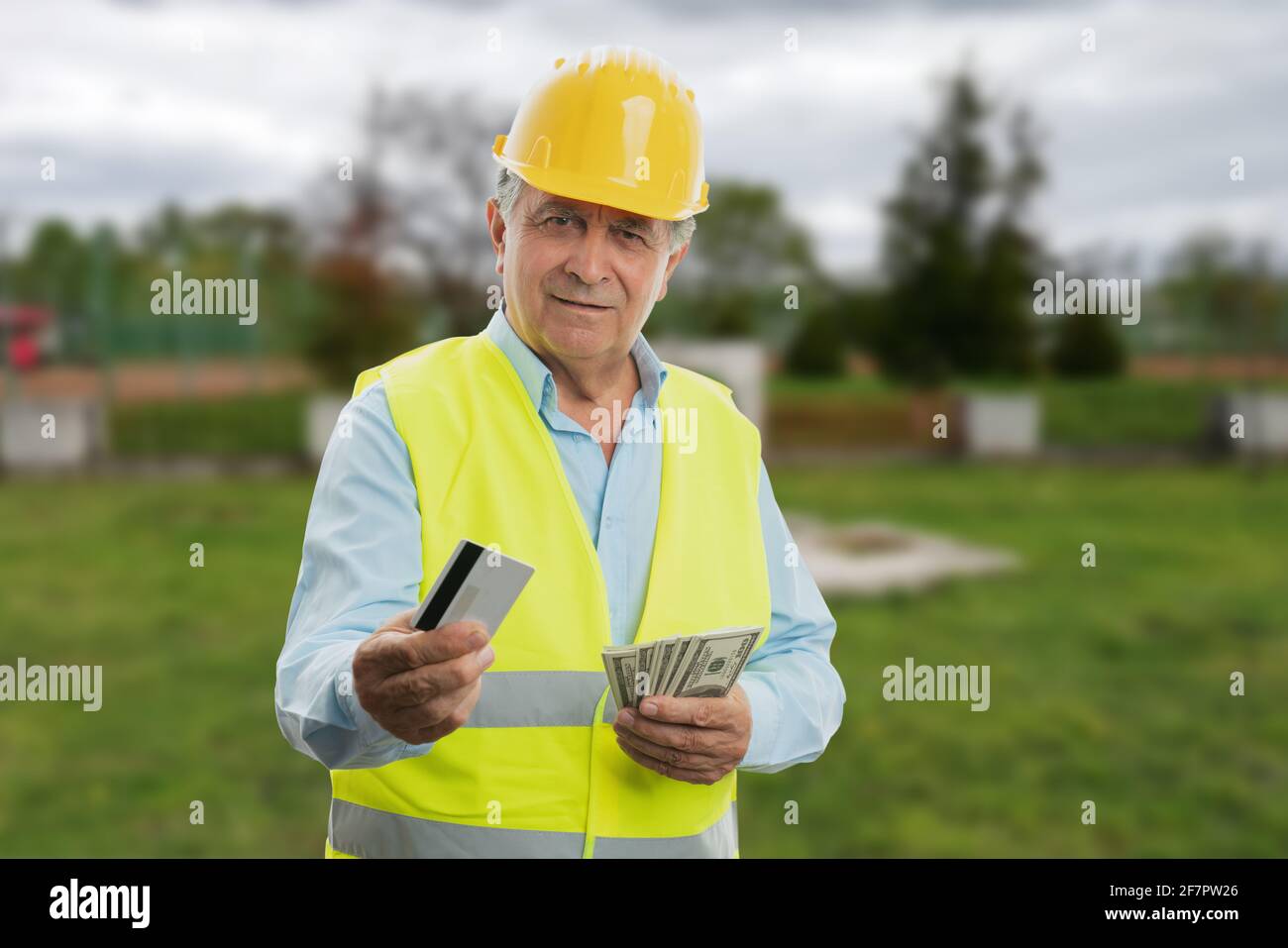Ancien constructeur mâle portant gilet fluorescent et tenue de casque de sécurité jaune argent comptant comme salaire et paiement par carte de crédit ou de débit concept de salaire Banque D'Images