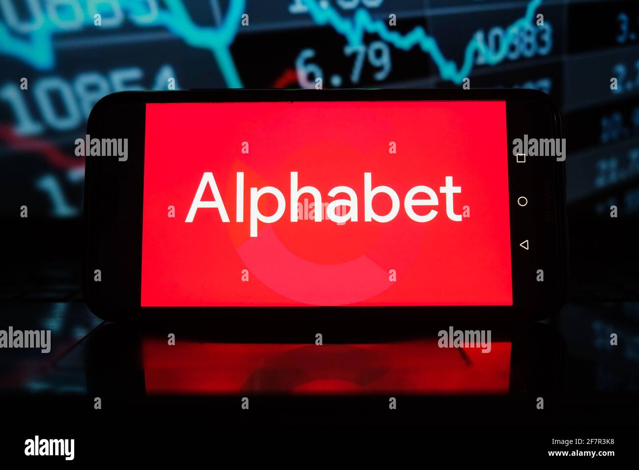 Sur cette photo, un logo Alphabet apparaît sur un smartphone avec des pourcentages boursiers en arrière-plan. Banque D'Images