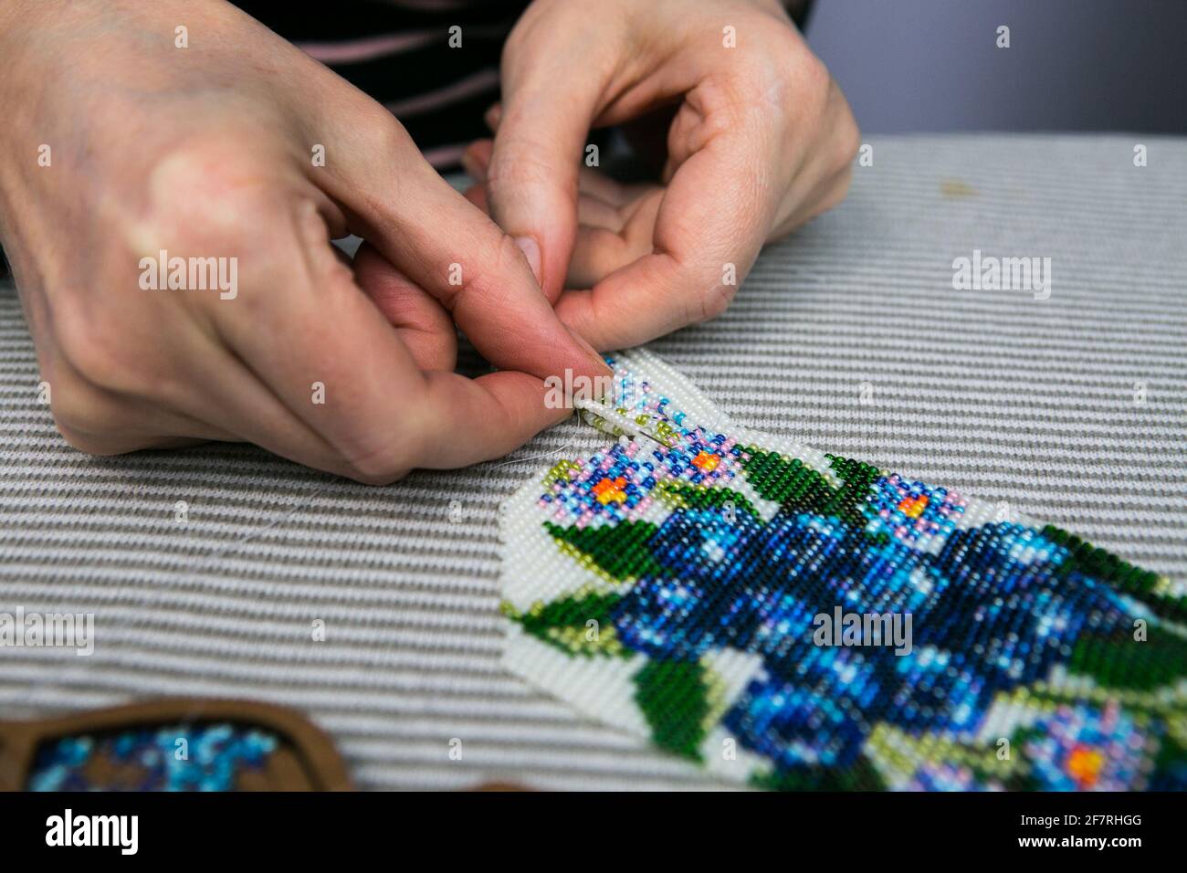 Tissage à partir de perles. Gros plan - les mains d'une femme sont en train de faire des perles sur un fil, faisant des bijoux. La femme aime tisser à partir de perles. Banque D'Images