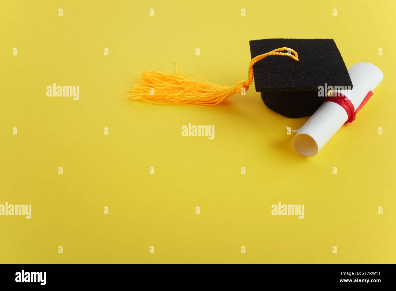 Chapeau universitaire avec diplôme sur fond jaune. Thème de la remise des diplômes Banque D'Images