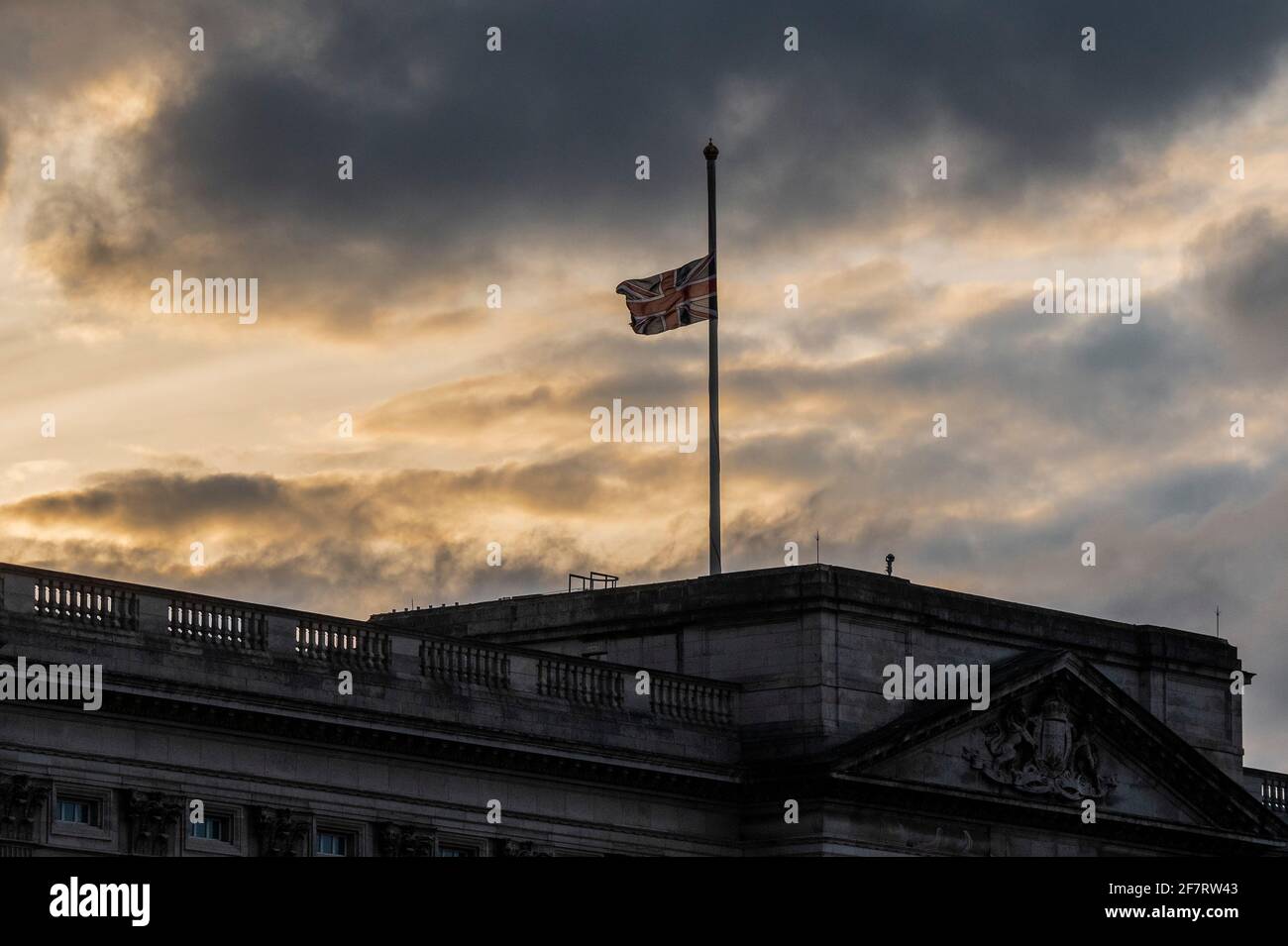 Londres, Royaume-Uni. 9 avril 2021. Le soleil se couche derrière le drapeau qui est en Berne - le prince Philip, duc d'Édimbourg, vient de mourir au château de Windsor. Ci-dessous, les gens posent des hommages floraux, au pied des rails de Buckingham Palace. Crédit : Guy Bell/Alay Live News Banque D'Images