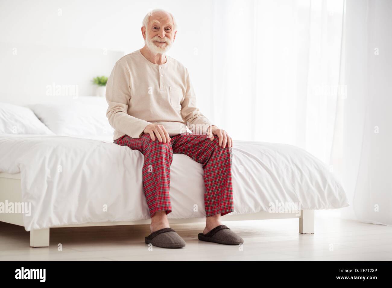Photo du corps complet de l'homme senior sourire heureux positif assis lit  maison intérieur vêtements pyjama pantoufles repos détente Photo Stock -  Alamy