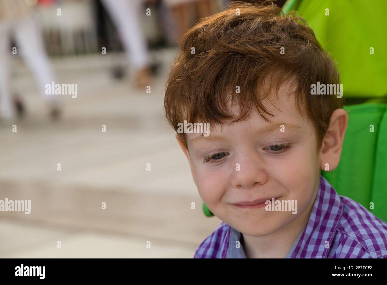 Détail d'un adorable garçon à tête rouge et yeux bleus assis dans une poussette verte par beau temps Banque D'Images