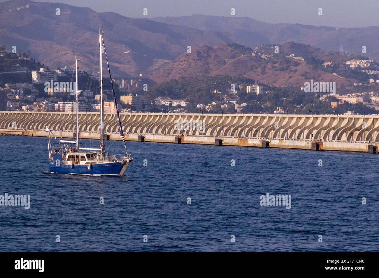 Un voilier bleu quittant le port de Malaga en face d'un amarrez avec la ville en arrière-plan Banque D'Images