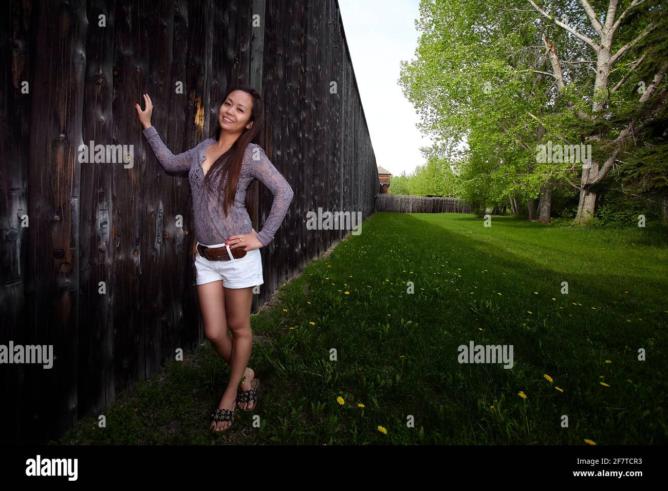 Femme asiatique pleine corps touriste avec main sur la taille penchée dans le mur de bois et regardant la caméra avec le sourire à fort Edmonton en Alberta, Canada Banque D'Images