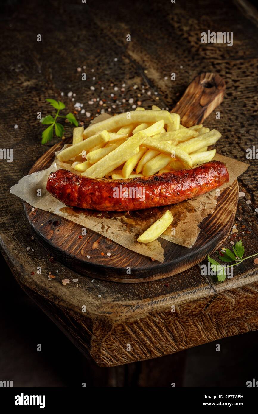 Concept de grill. Saucisse savoureuse grillée et rôtie avec frites sur l'ancienne planche à découper en bois. Banque D'Images