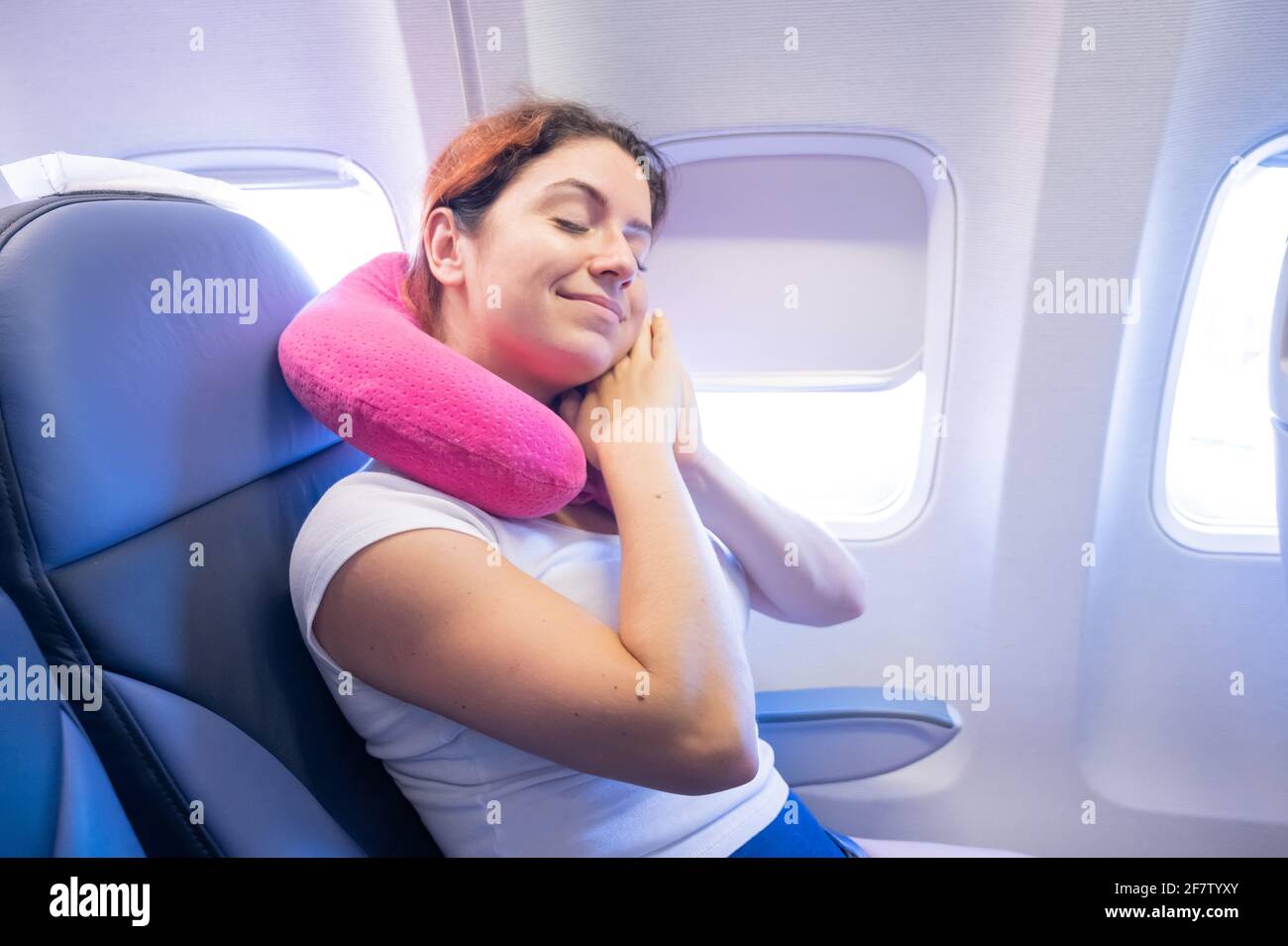 Portrait d'une jeune femme de race blanche dans un avion avec un oreiller de voyage autour de son cou Banque D'Images