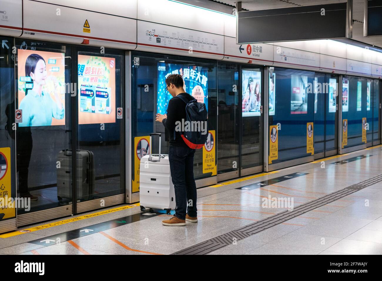 Hong Kong, Chine - novembre 2019: Jeune asiatique avec bagages regardant le téléphone, attendant à la station MTR / station de métro à Hong Kong Banque D'Images