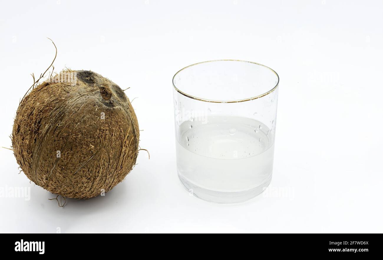 Photographie isolée d'une noix de coco et à côté d'elle un verre d'eau de coco sur fond blanc Banque D'Images