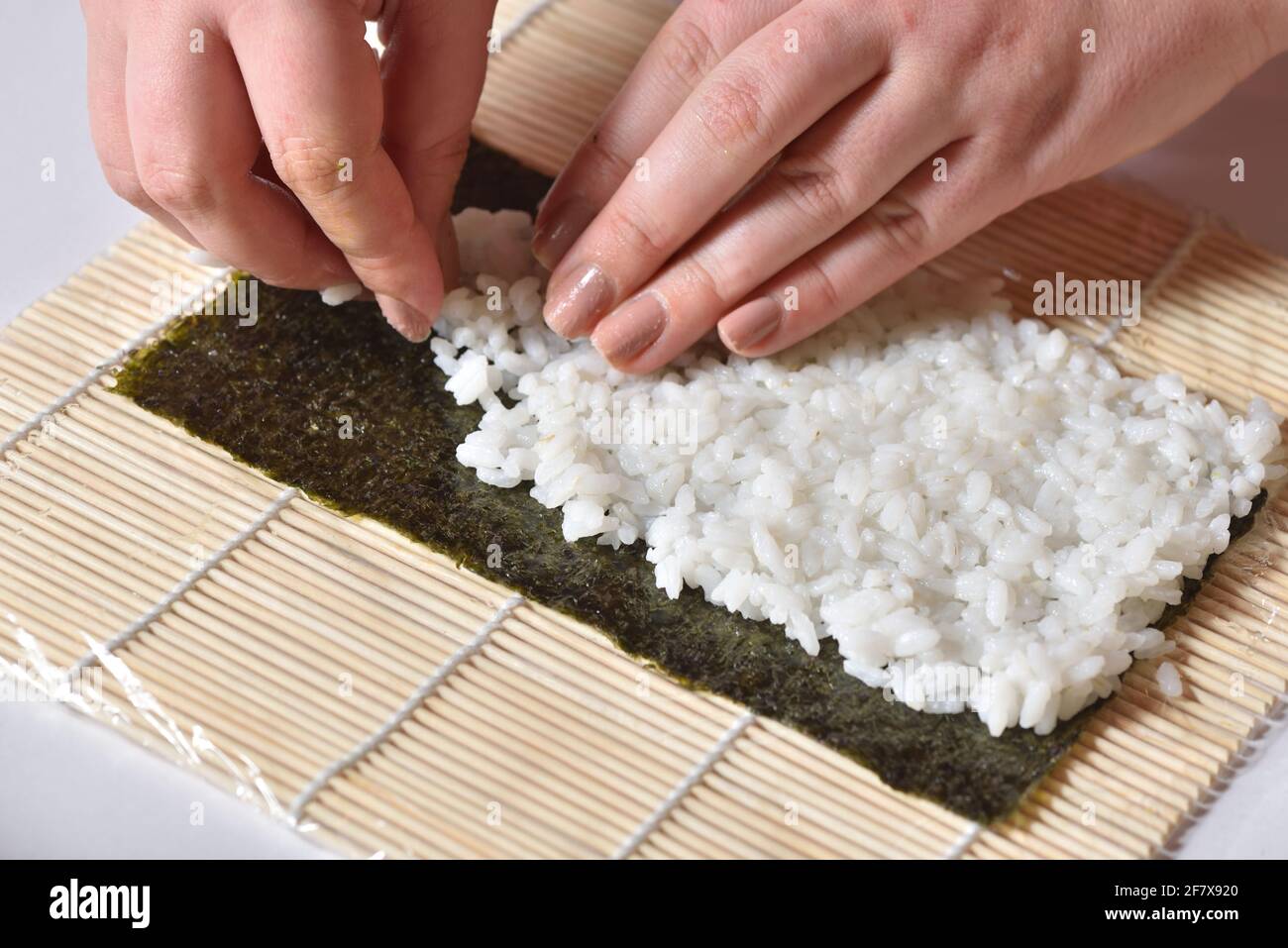 Les mains des femmes préparent un rouleau de sushi maison et y reposent le riz feuille de nori Banque D'Images