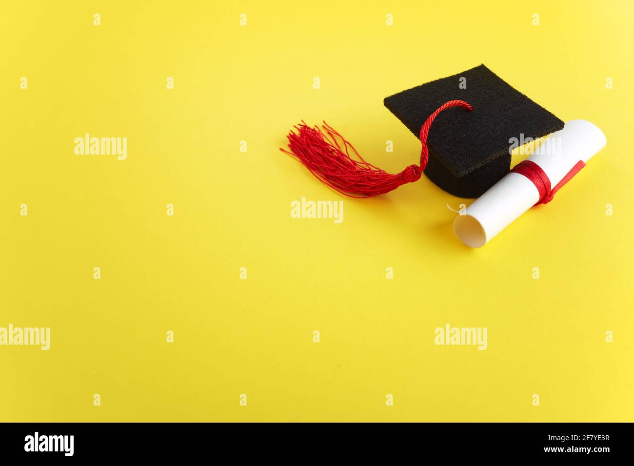 Chapeau universitaire avec diplôme sur fond jaune. Thème de la remise des diplômes Banque D'Images