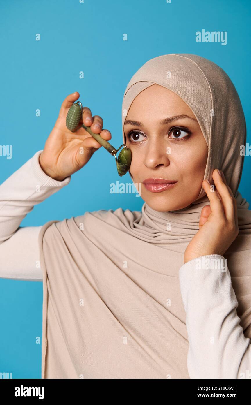 Une jeune belle femme musulmane avec tête couverte dans le hijab faisant un  massage facial avec un rouleau de jade Photo Stock - Alamy
