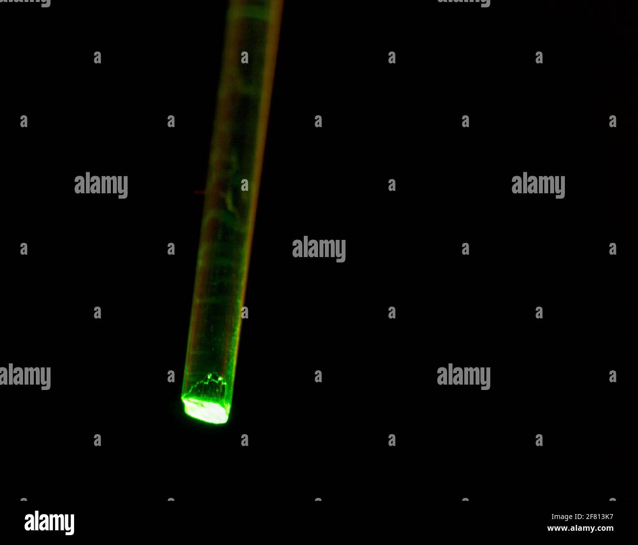 Fibre optique en plastique transmettant une lumière verte sur un fond sombre, illustrant la transmission de lumière par fibre optique et la technologie optique Banque D'Images