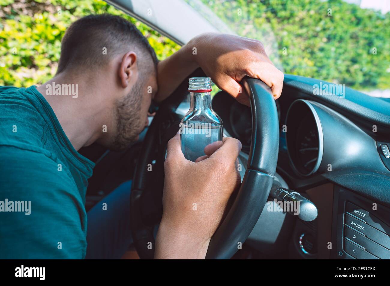 Homme ivre dormant sur le volant dans sa voiture avec une bouteille de vodka dans ses mains. Conducteur ivre Banque D'Images