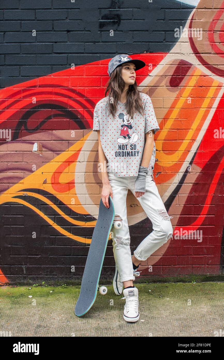 Adolescente avec planche à roulettes debout près d'un mur urbain avec graffiti coloré à Sorvitch à Londres , Royaume-Uni . Banque D'Images