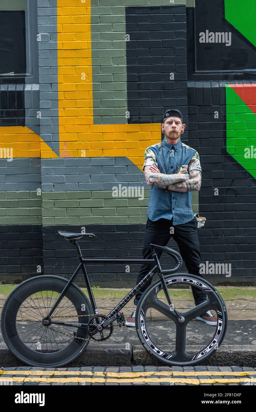 Un jeune homme hippster avec son vélo sur fond de mur de graffiti. Banque D'Images