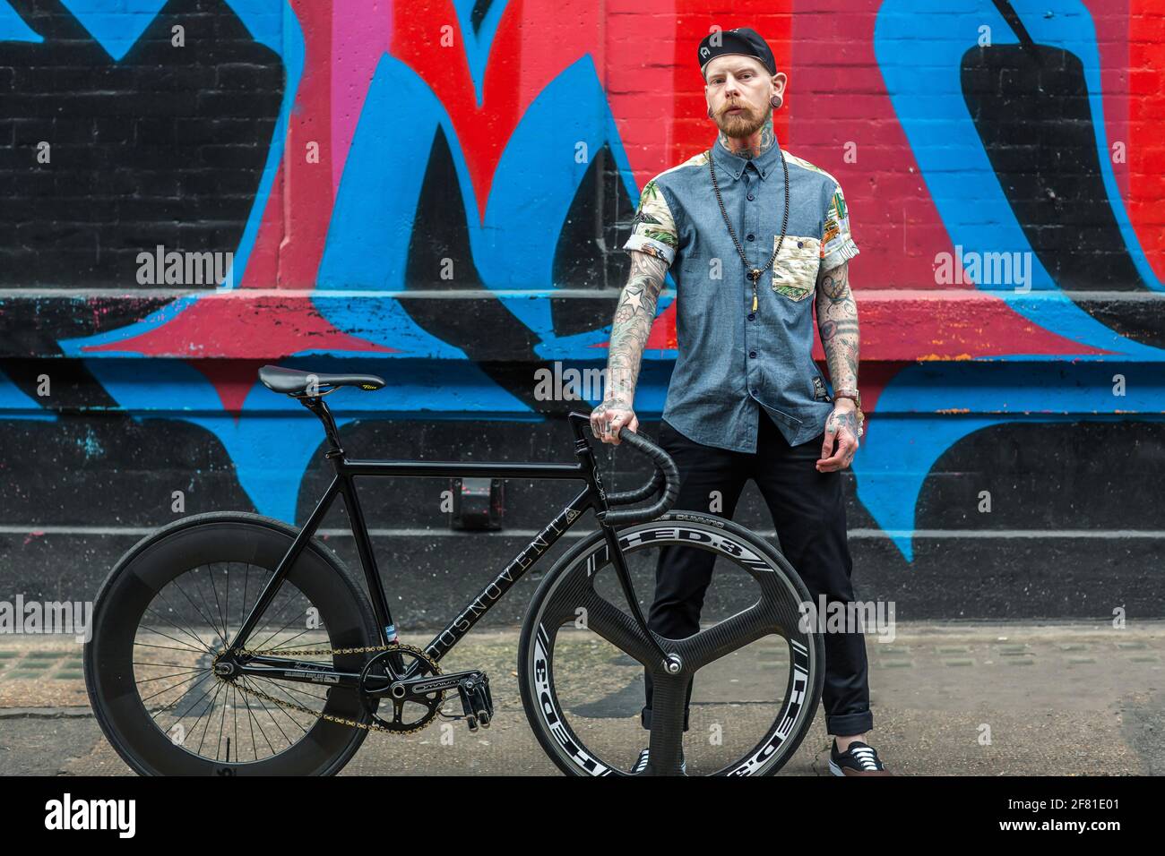 Un jeune homme hippster avec son vélo sur fond de mur de graffiti. Banque D'Images