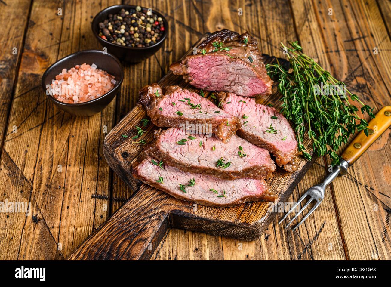 Tranches rares de rôti de boeuf sirloin à trois pointes steak bbq sur une planche à découper en bois. fond en bois. Vue de dessus Banque D'Images